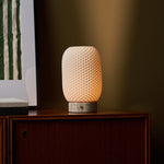 Cordless table lamp, Aurora Silver Travertine and Porcelain design, glowing on a beige studio backdrop