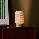 Cordless table lamp, Aurora Silver Travertine and Porcelain design, glowing on a beige studio backdrop