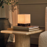 Barent marbre Emperador Dark lampe de table rechargeable Tavellio - sur guéridon rond en travertin - à côté d'un olivier en pot et de livres