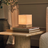 Barent travertin Classic lampe de table rechargeable Tavellio - posée sur des livres empilés près d'un olivier - ambiance salon chaleureuse