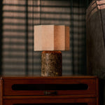 Cordless table lamp Bonnard Large in dark marble glowing on a wood nightstand beside striped window blinds