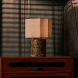 Cordless table lamp Bonnard Large in dark marble glowing on a wood nightstand beside striped window blinds