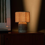 Rechargeable table lamp Bonnard Large by Tavellio in grey travertine glowing warmly against an amber wall