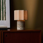 Cordless table lamp Bonnard Large in silver travertine glowing on a walnut cabinet beside striped wall art