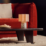 Cordless Bonnard table lamp glowing on a dark coffee table beside a rust red velvet sofa