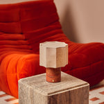 Bonnard cordless table lamp in Red Travertine stone glowing on a marble side table beside a red velvet sofa