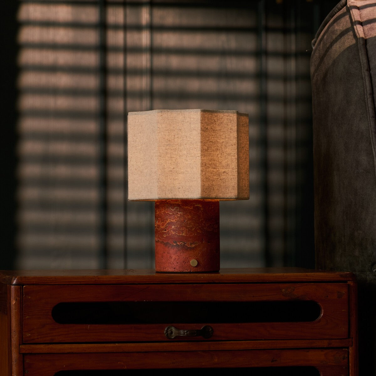 Tavellio Bonnard cordless table lamp in Red Travertine stone glowing warmly on a teak sideboard at dusk