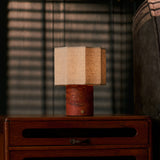 Tavellio Bonnard cordless table lamp in Red Travertine stone glowing warmly on a teak sideboard at dusk