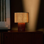 Bonnard rechargeable table lamp in Red Travertine stone lit atop a teak sideboard beside framed wall art