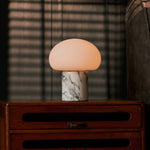 Rechargeable table lamp with an Arabescato marble base glowing on a dresser, blinds casting striped shadows