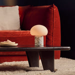 Cordless table lamp glowing on a dark coffee table beside a red velvet sofa and cream rug