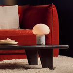 Codde Blue Calcite marbre lampe de table rechargeable Tavellio – allumée sur une table basse foncée devant un canapé en velours rouge