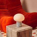 Codde Blue Calcite marbre lampe de table rechargeable Tavellio – gros plan sur un cube en pierre beige devant un fauteuil orange