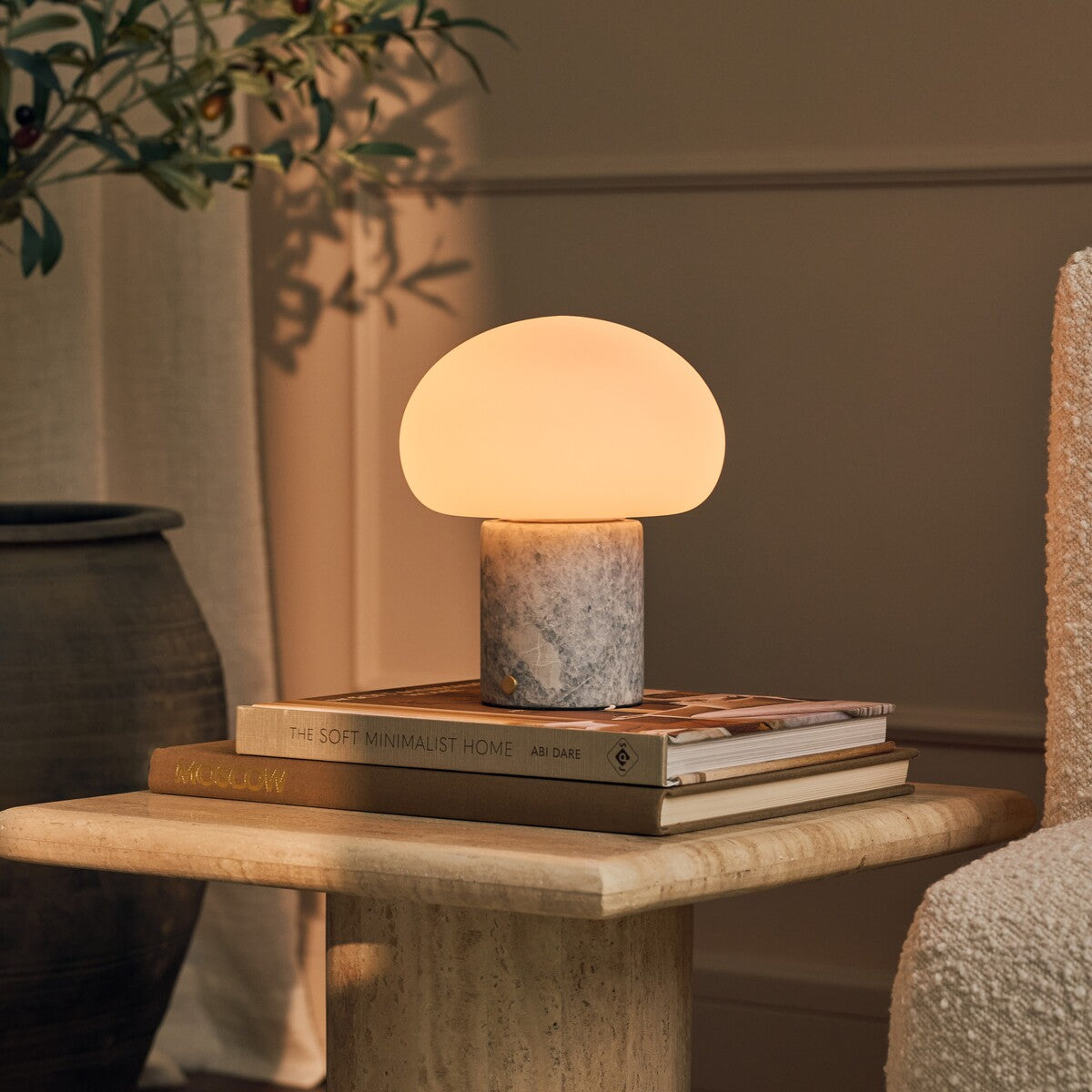 Codde Blue Calcite marbre lampe de table sans fil Tavellio – posée sur une pile de livres sur une table en travertin, plante à côté