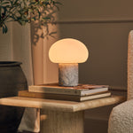 Codde Blue Calcite marbre lampe de table sans fil Tavellio – posée sur une pile de livres sur une table en travertin, plante à côté