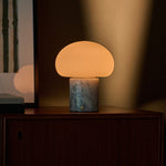 Codde Blue Calcite marbre lampe de table rechargeable Tavellio – allumée sur un buffet en bois, cadre rayé vert visible à gauche
