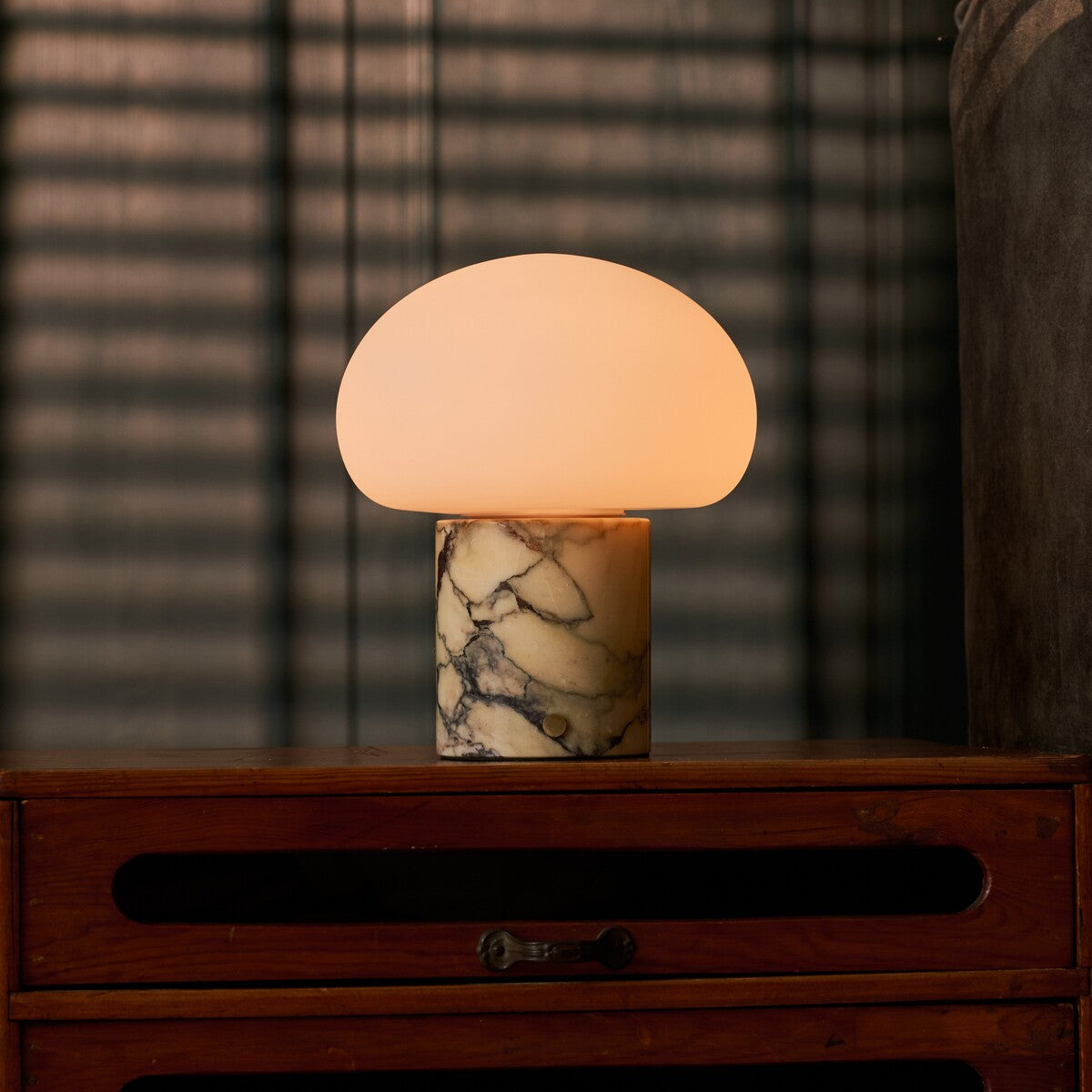 Codde marbre jaune Calacatta Vionaro lampe de table rechargeable Tavellio – posee sur une commode au crepuscule – ombres rayees d un store venitien en fond