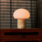 Rechargeable table lamp with honey onyx marble base glowing on a wooden dresser in a dim bedroom with blinds