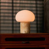 Rechargeable table lamp with honey onyx marble base glowing on a wooden dresser in a dim bedroom with blinds