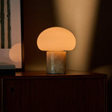 Tavellio cordless table lamp with honey onyx marble base glowing on a wooden cabinet beside framed wall art