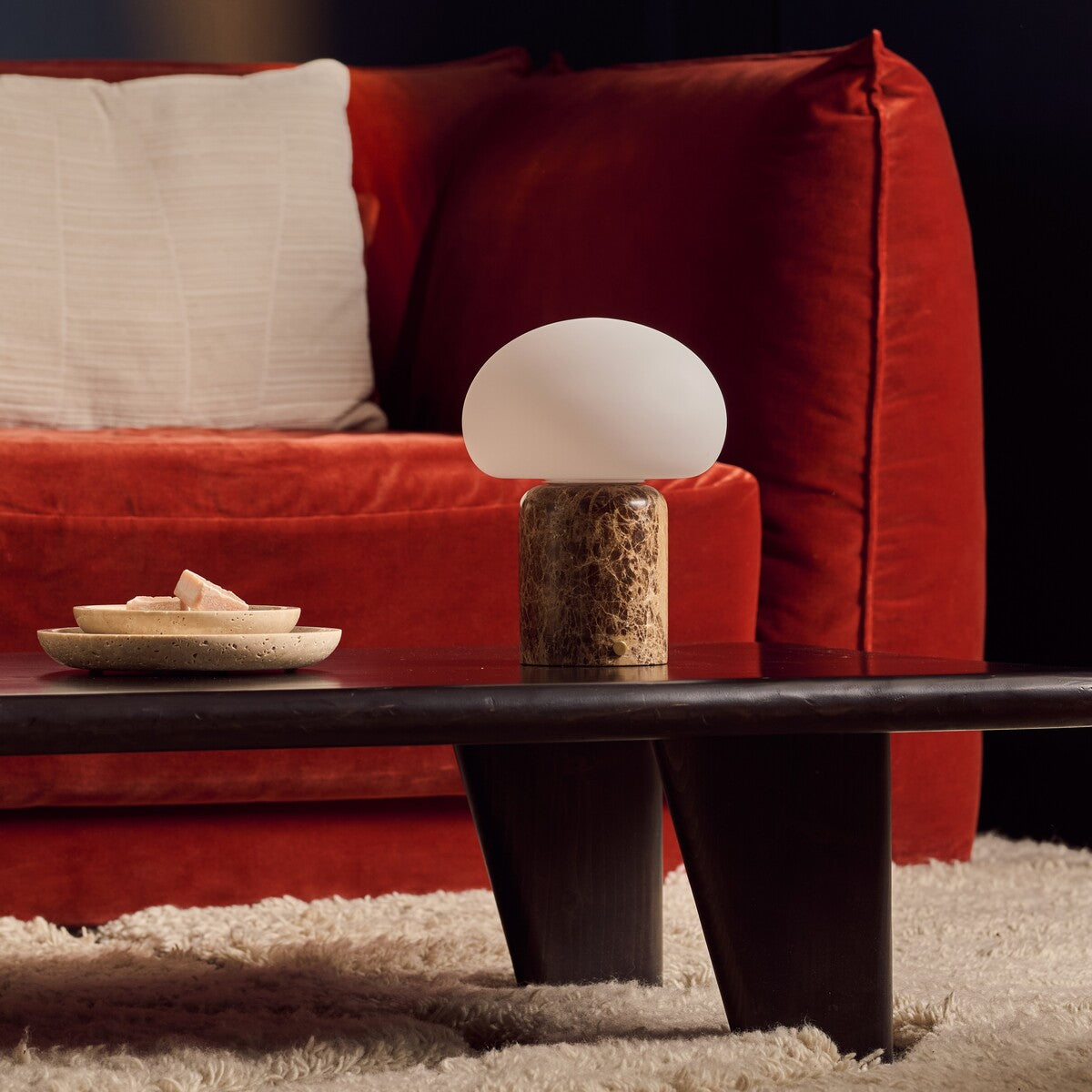Coddé Large marbre Emperador foncé lampe de table rechargeable Tavellio – table basse noire devant un canapé en velours rouge – coupelle en travertin