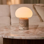 Coddé Large travertin gris lampe de table sans fil Tavellio – posée sur une table en marbre rose près d'un canapé crème – coussin à rayures