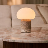 Coddé Large travertin gris lampe de table sans fil Tavellio – posée sur une table en marbre rose près d'un canapé crème – coussin à rayures