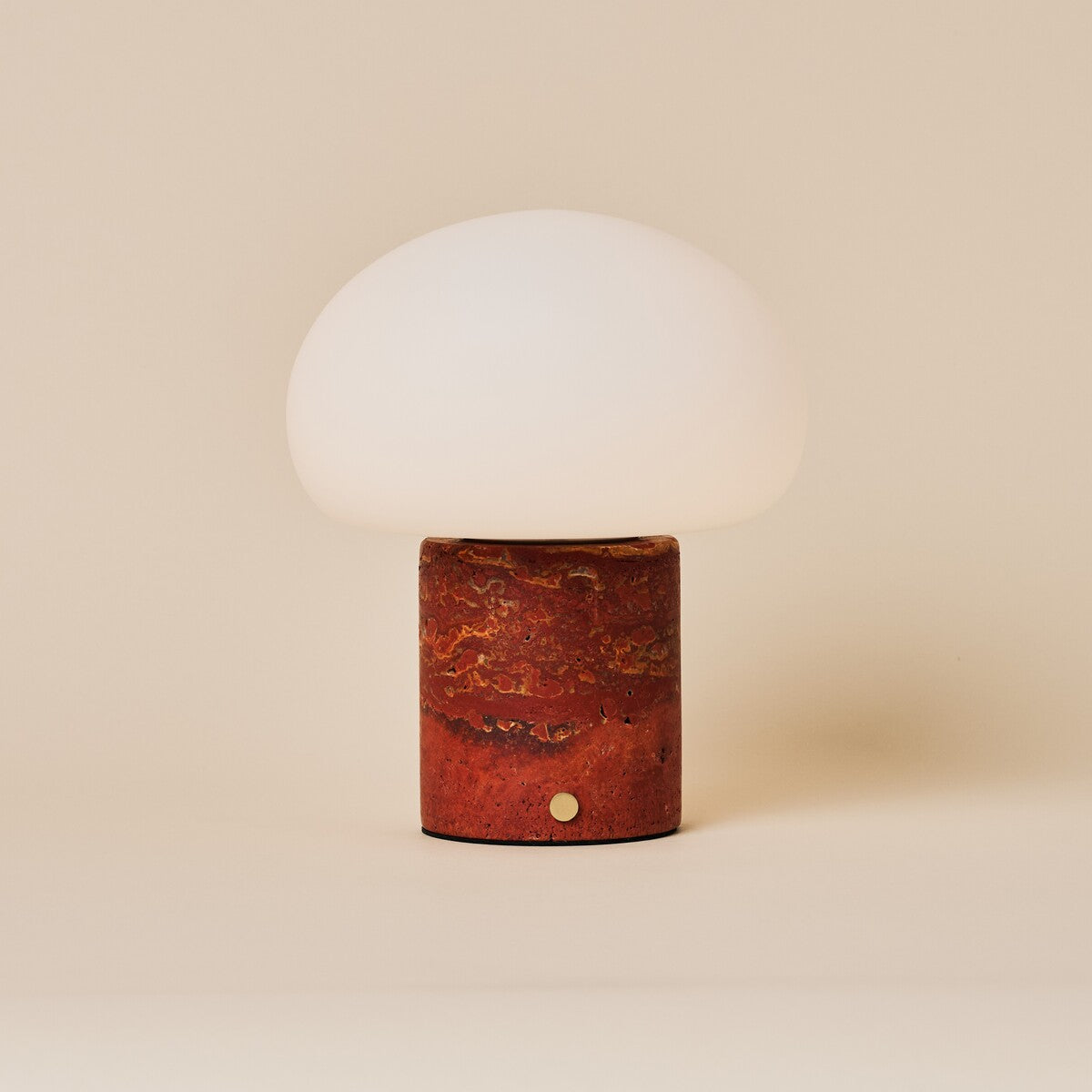 Rechargeable table lamp with red travertine base and opal glass dome shade on a plain backdrop