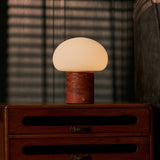 Rechargeable table lamp with red travertine base glowing on a wooden dresser in a dim bedroom with blinds
