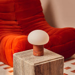 Cordless table lamp with red travertine base glowing on a travertine cube beside a burnt-orange sofa