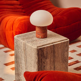 Rechargeable table lamp with red travertine base on a travertine plinth with an orange corduroy cushion in view