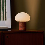 Tavellio cordless table lamp with red travertine base glowing on a wooden cabinet beside framed wall art