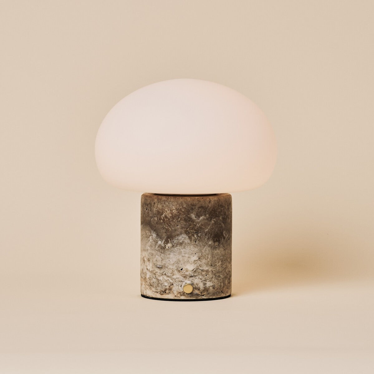 Cordless table lamp with a rounded glass shade on a Silver Travertine stone base, studio shot on beige