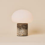 Cordless table lamp with a rounded glass shade on a Silver Travertine stone base, studio shot on beige