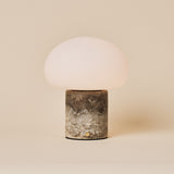 Cordless table lamp with a rounded glass shade on a Silver Travertine stone base, studio shot on beige