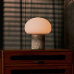 Tavellio rechargeable table lamp glowing on a wooden dresser, striped shadows cast by the blinds