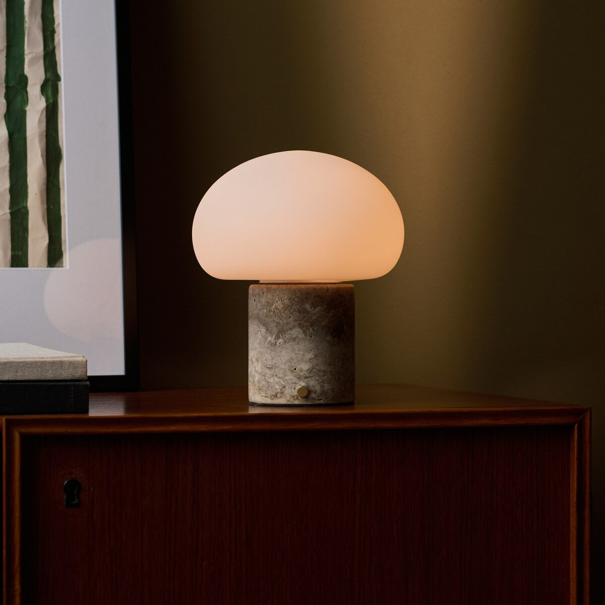 Rechargeable table lamp with a Silver Travertine base glowing on a dark wood credenza beside a striped print