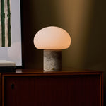 Rechargeable table lamp with a Silver Travertine base glowing on a dark wood credenza beside a striped print