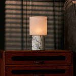 Cuyp Arabescato Marble cordless table lamp on a bedroom nightstand with venetian blinds and plaid throw