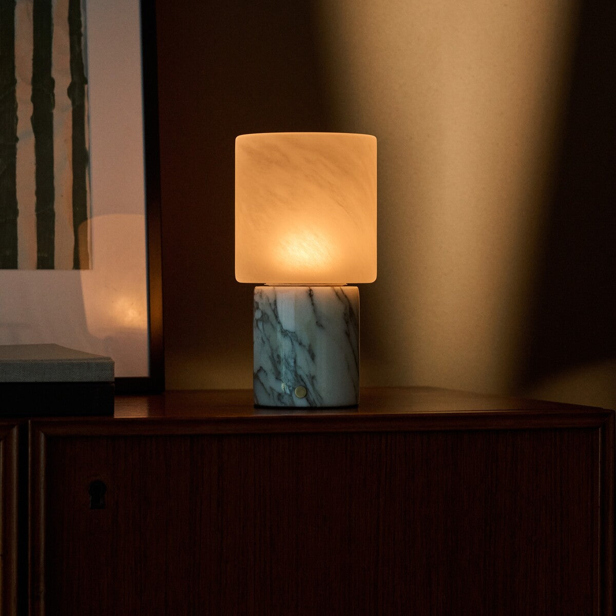 Tavellio Cuyp Arabescato Marble table lamp glowing on a wood cabinet with a keyhole drawer nearby
