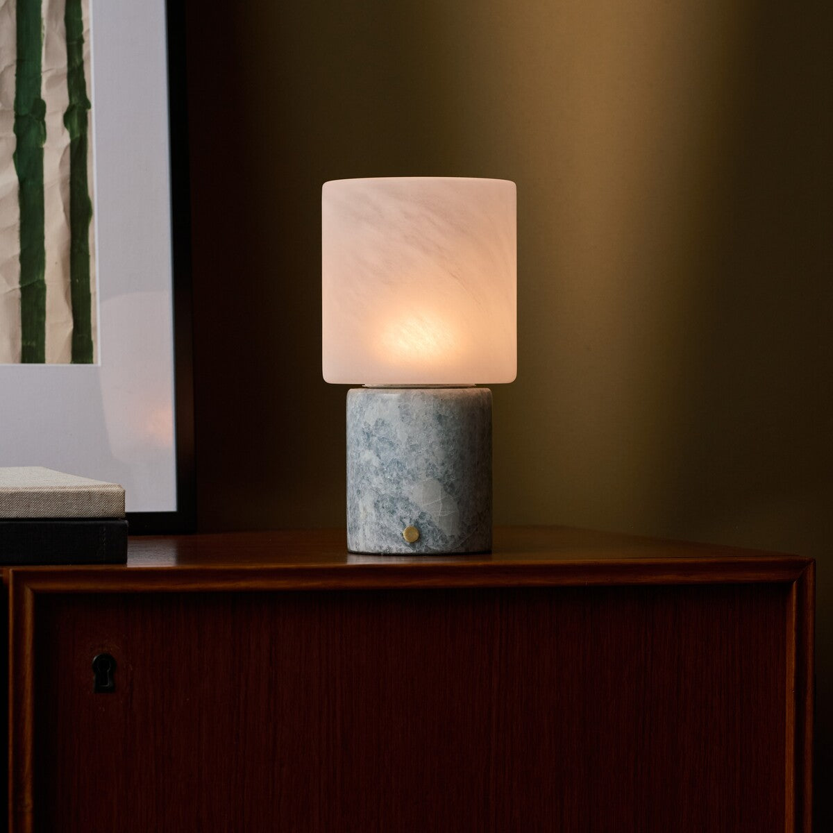 Cordless table lamp with blue calcite marble base lighting a walnut cabinet in a dim room