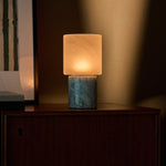 Rechargeable table lamp with blue-grey marble base glowing on a dark wood cabinet at night