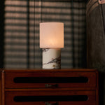 Cuyp table lamp with white marble base and square glass shade glowing warmly at bedside