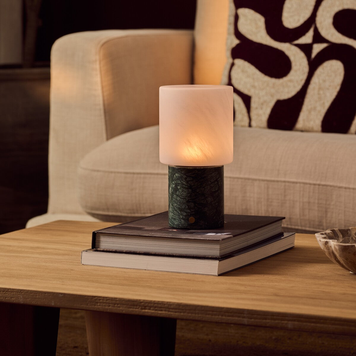 Cuyp Green Marmor kabellose Tischlampe Tavellio – auf gestapelten Büchern auf Holztisch – gemustertes Kissen im Hintergrund
