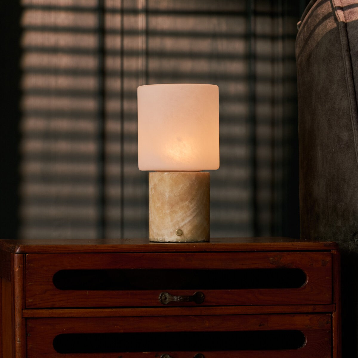 Tavellio rechargeable table lamp with honey onyx base on a nightstand under blind-cast shadows