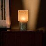 Cordless table lamp with honey onyx marble base glowing against a striped green artwork