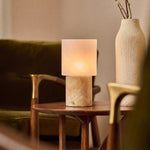 Cordless table lamp with honey onyx marble base glowing beside a ceramic vase and olive branch