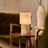 Cordless table lamp with honey onyx marble base glowing beside a ceramic vase and olive branch