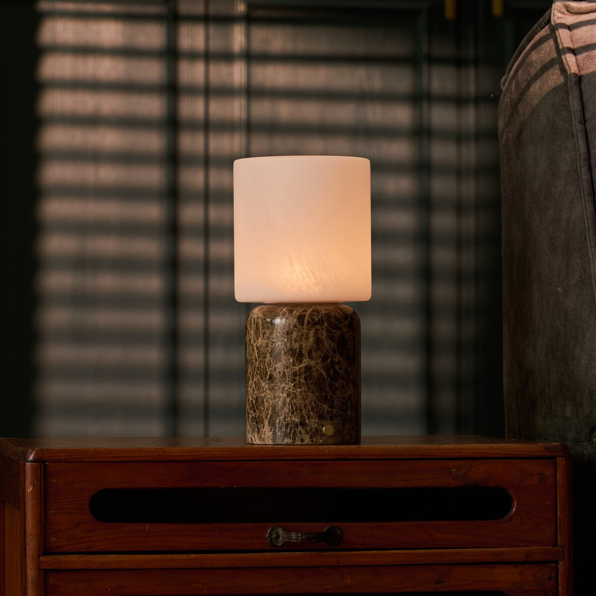 Cordless table lamp Cuyp Large in Emperador dark marble casting warm light beside striped window blinds