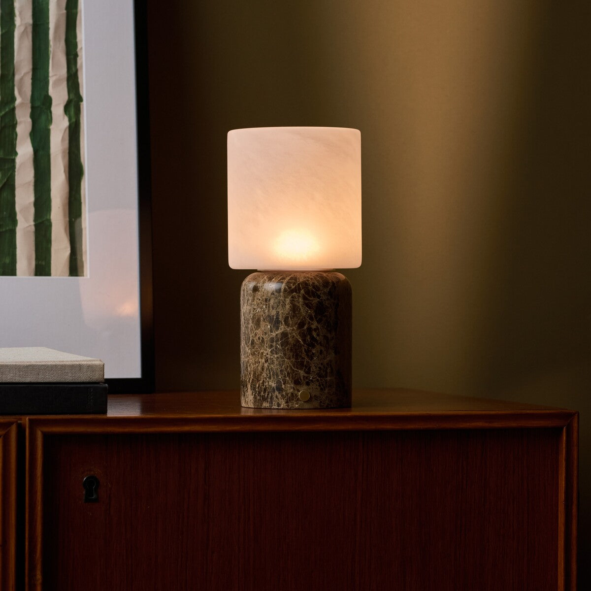 Rechargeable table lamp Cuyp Large in Emperador dark marble glowing on a wood cabinet against an olive wall